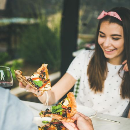 Couple eating pizza al fresco with wine with woman smiling, square crop