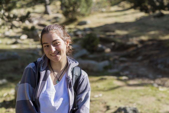 Happy young female standing in green woods with boulders on ground