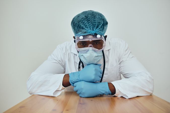 Thoughtful Black male doctor in ppe gear leaning on table