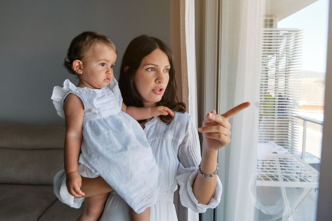 Mother and little daughter looking out window at home