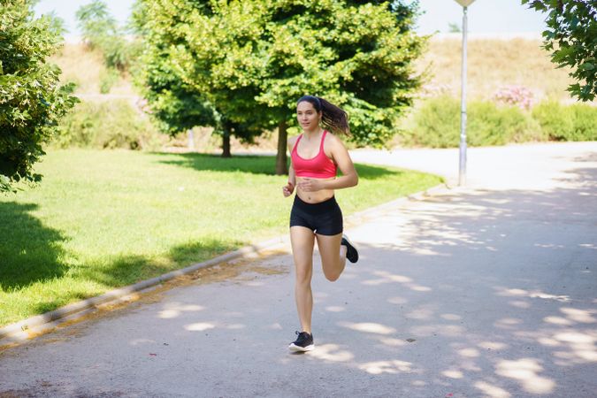 A young woman is jogging in the park, enjoying nature, exercising, and embracing a healthy lifestyle