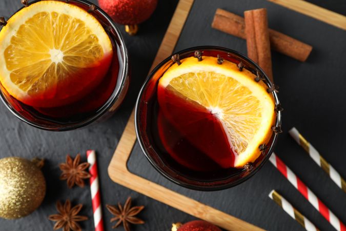 Glasses of tasty mulled wine and christmas baubles on dark background, close up