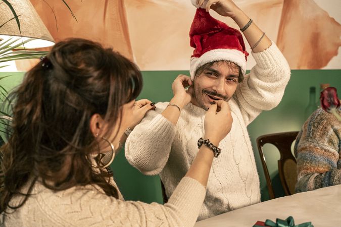 Joyful young man laughing while playfully wearing a Santa hat at a Christmas party.