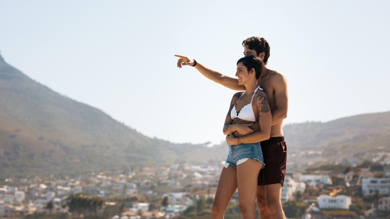 Couple standing on a hilltop and looking at the city with mountains in the background