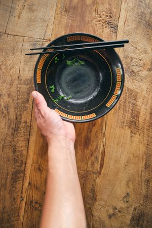 Crop person with ornamental bowl and chopsticks on desk