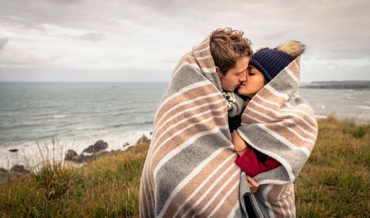 Couple kissing under blanket with choppy ocean in the background