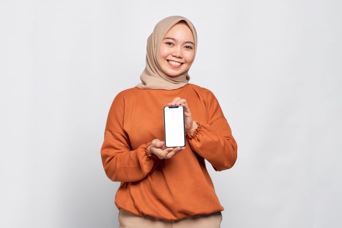 Confident Muslim woman smiling while holding up smart phone with mock up screen with both screen