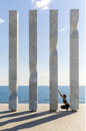 Side view of female stretching on sculpture by the sea