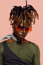 Portrait of a serious young man in green with dreadlocks and red sunglasses, isolated on pink