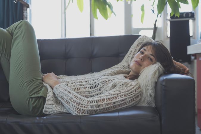 Female in wooly sweater relaxing on leather couch in living room