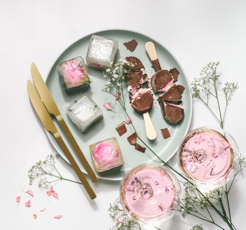 Ice cream popsicles with chocolate on plate with gypsophila,  wine glasses with rose wine, ice cubes and golden knifes