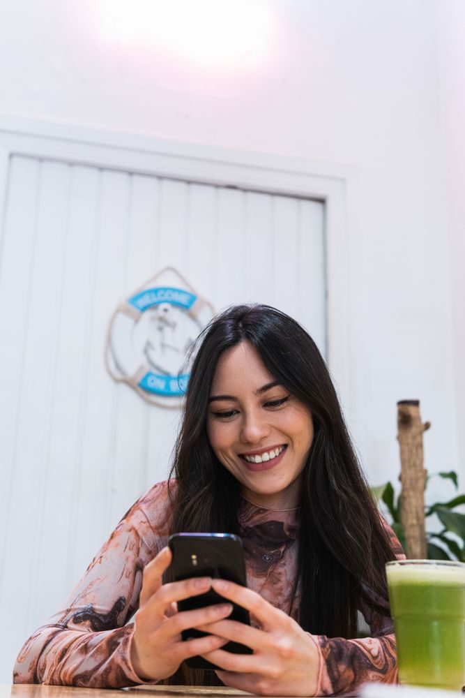 Smiling woman using smartphone at table in bar