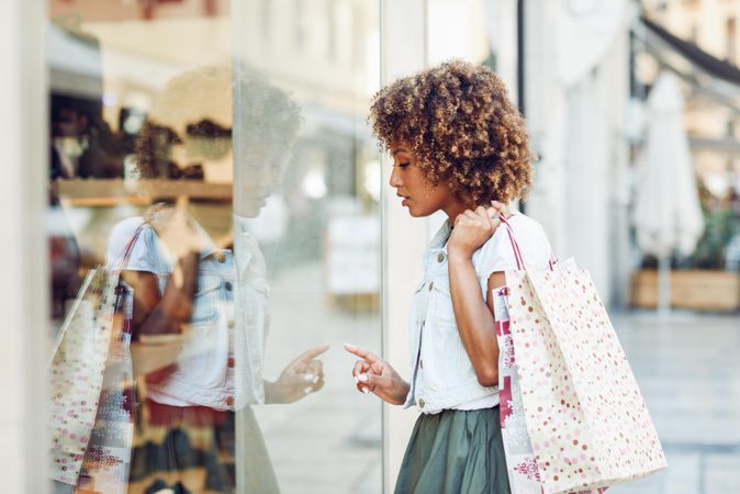 Pretty Black woman pointing at a shop window and holding shopping bags