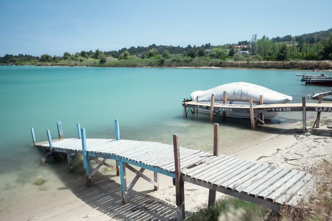 Wooden jetty with lifebuoys and sailing blue boat in calm water