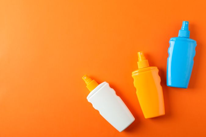 Flat lay composition with sunscreen sprays on color background. Space for text