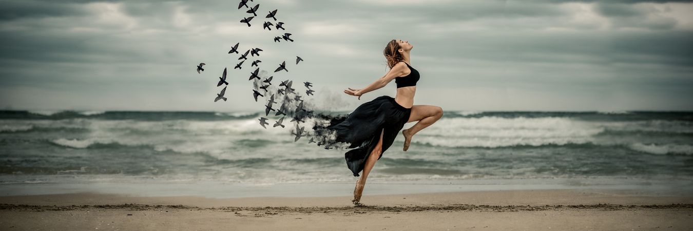 Young woman dancing with birds near sea