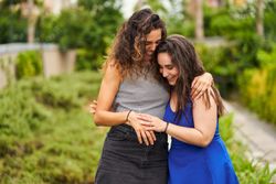 Two smiling friends embrace while walking in the park