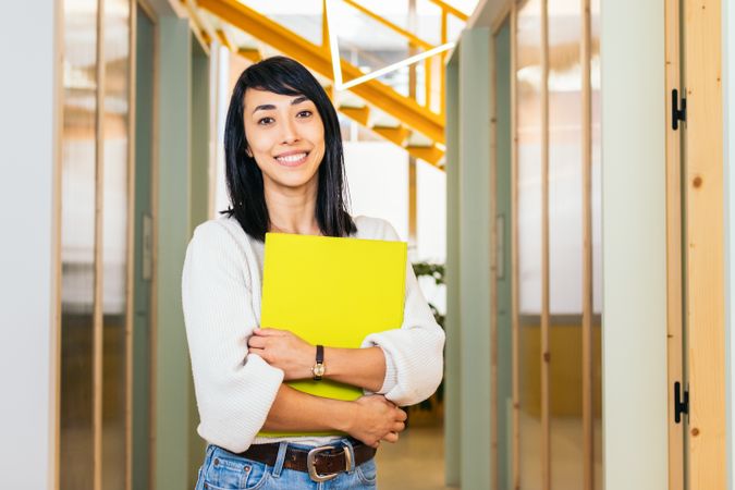 Portrait of smiling Asian woman looking at camera holding folder in modern office