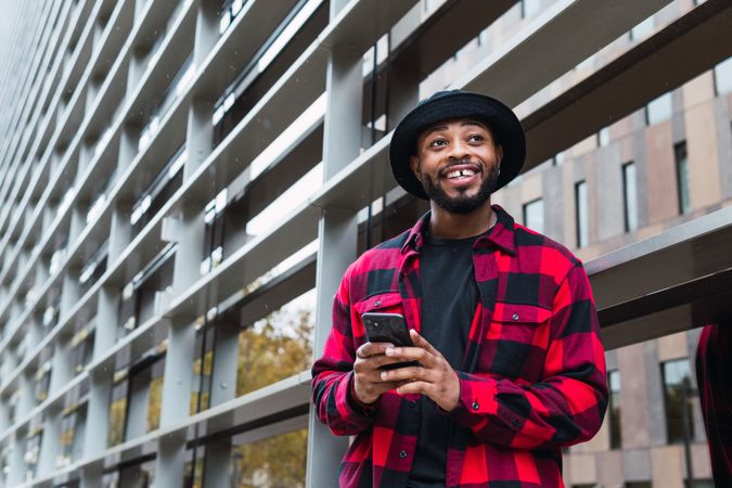 Cheerful Black male with smartphone in contemporary building