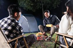 Asian Young Man Grilling Corn on Campfire
