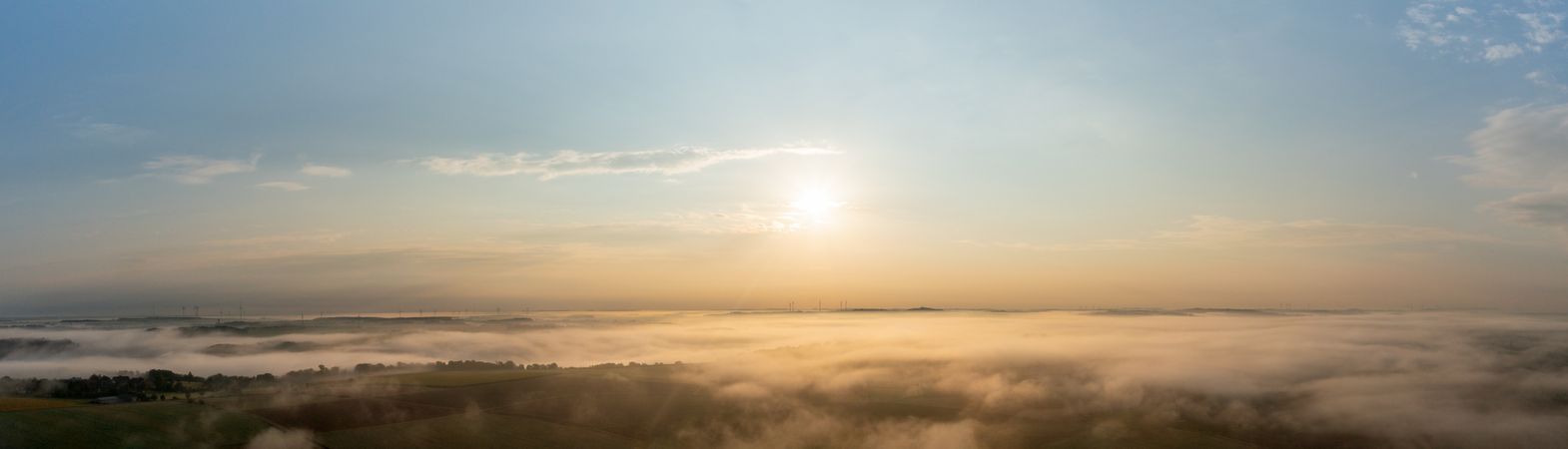 Drone panorama with golden light illuminating foggy agricultural fields and rolling hills