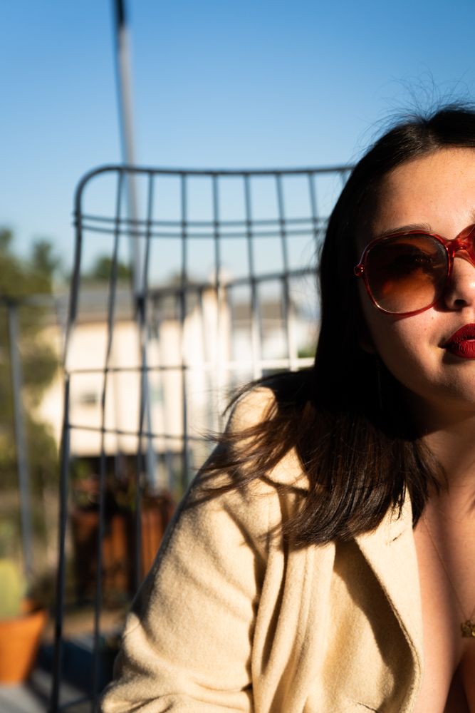 Cool young woman sitting on patio with sunglasses half in the shade