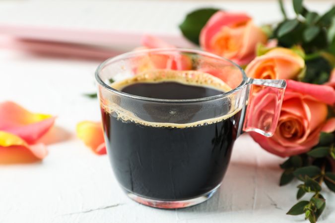 Cup of coffee and pink roses on neutral background, closeup