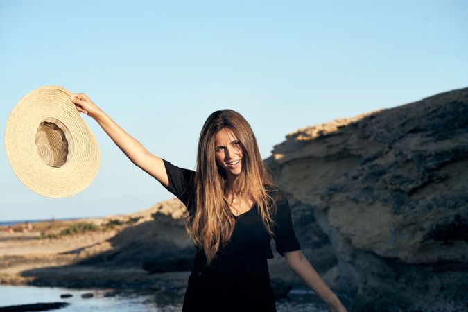 Cheerful woman holding hat in air