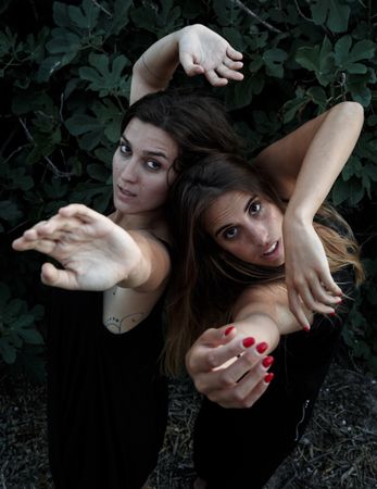 Young women posing near green bush