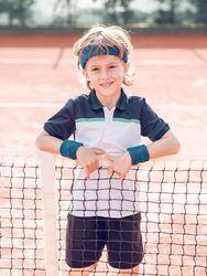 Cute sporty kid smiling at camera while standing on tennis court