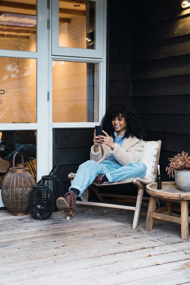 Cheerful Black woman browsing smartphone on terrace