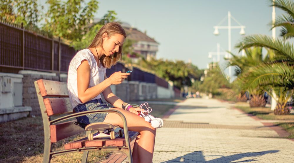 Young girl with skateboard and headphones looking smartphone