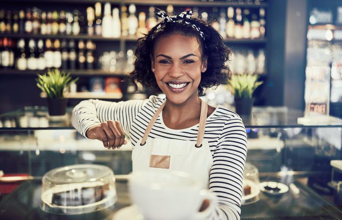 Smiling woman presenting a cup of coffee in front of a modern bar