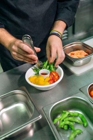 Unrecognizable chef hands preparing poke bowl with salmon and fresh vegetables in restaurant kitchen
