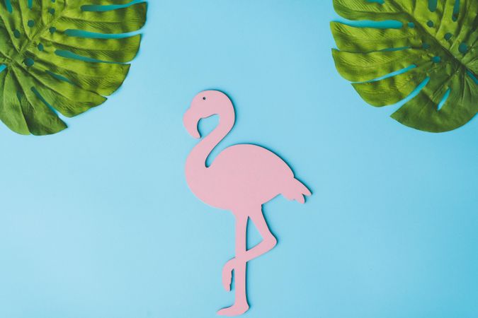 Pink flamingo shape with green tropical leaves on bright blue background