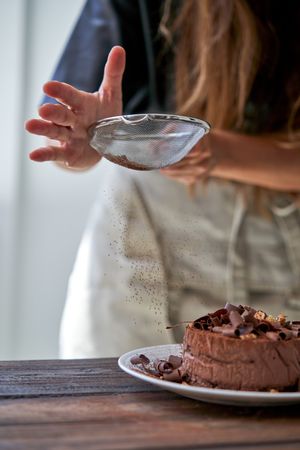 Woman sprinkling cocoa powder on cake