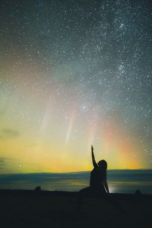 Woman doing yoga near sky in stars and polar lights at night