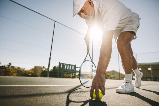 Active man picking up ball from tennis court