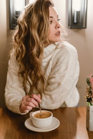 Elegant woman mixing coffee in cafe