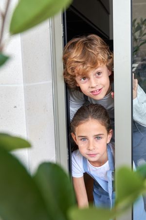 Children looking out of glass doorway of house