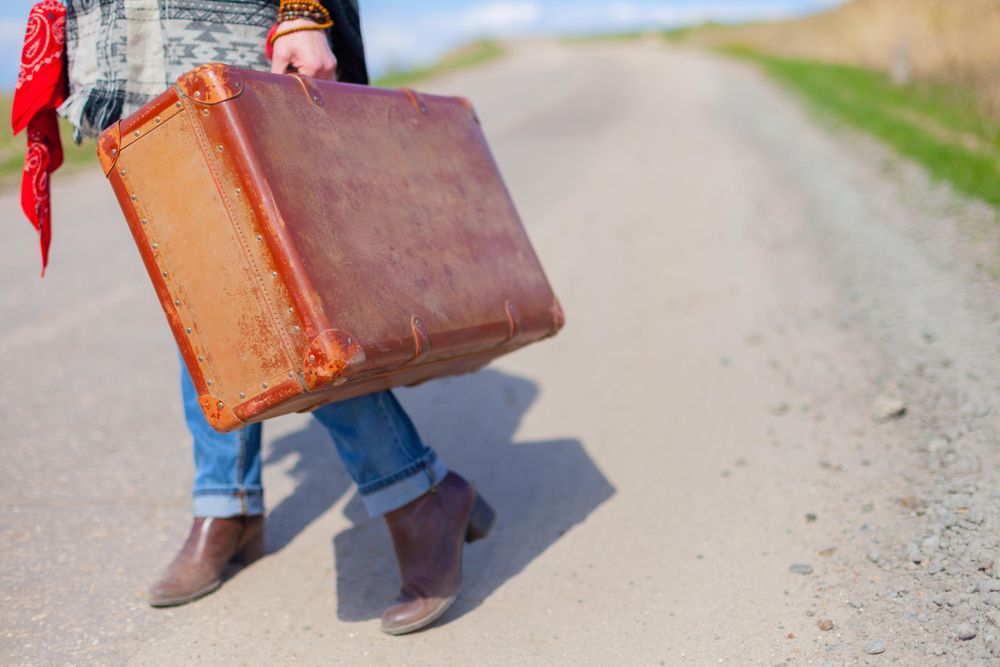 Person holding suitcase and standing on the road