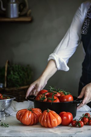 Woman holding pot with red fresh tomatoes on table