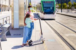 Mother and daughter waiting for tram with scooter