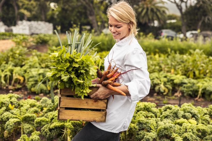 Smiling woman chef carrying a crate full of freshly picked vegetables on an organic farm