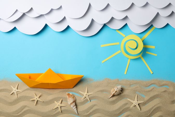 Paper clouds, sun and boat, sand with starfishes on blue background. Vacation