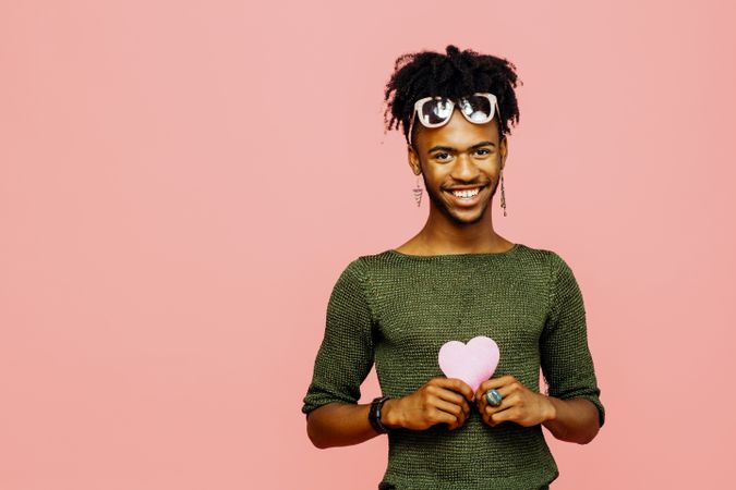 Portrait of a smiling young man holding a pink heart, isolated on pink studio background