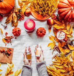 Autumn skin care ´beauty products. Women hand holding cosmetic bottles at white background with fall leaves, candles, pumpkins and hot chocolate. Top view with copy space. Beauty lifestyle