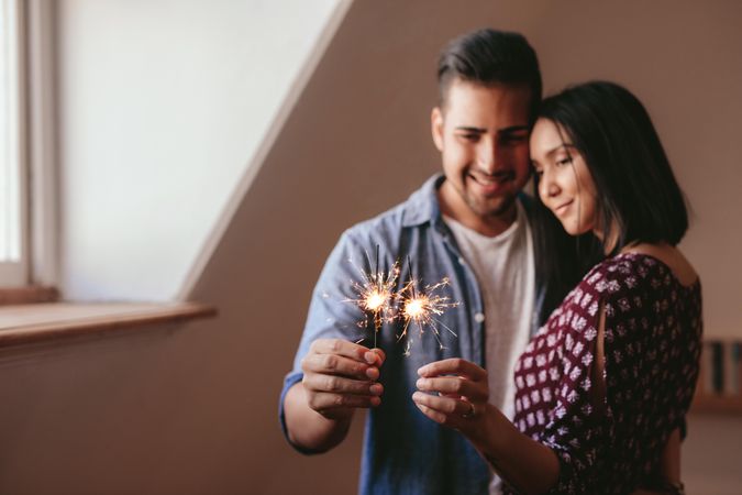 Happy young man and woman holding sparklers at home