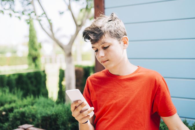 Teenage boy outside wearing red t-shirt using phone