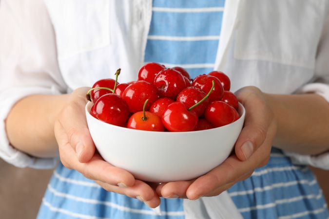 Woman holds bowl with fresh red cherry, close up